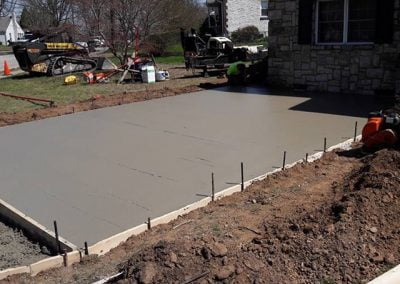 Freshly poured concrete slab next to a house under construction on a clear day.