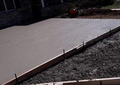 Freshly poured concrete slab with wooden frames and construction tools nearby.