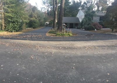 Residential house with large driveway surrounded by trees and fallen leaves.