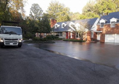 Large brick house with a circular driveway, surrounded by trees; a white truck is parked on the left side.