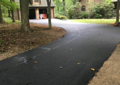 Freshly paved driveway leading to a house surrounded by trees.