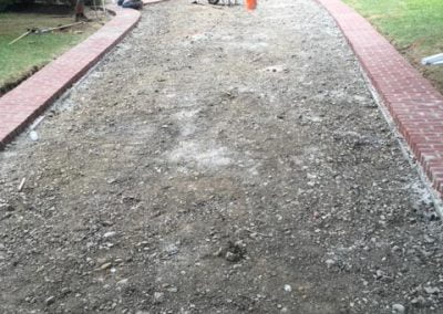 Workers leveling a gravel path with brick edging in front of a house.