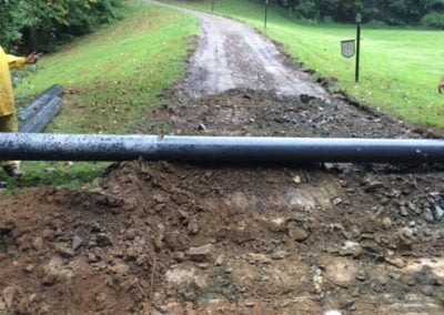 Dirt road under construction with a pipeline and surrounding green trees.