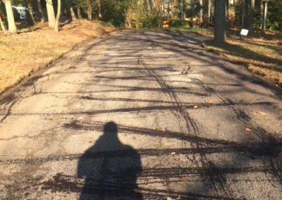 Shadow of a person on a cracked asphalt road lined with trees on a sunny day.