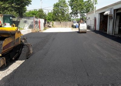 Paving crew working on a freshly laid asphalt driveway beside a garage.
