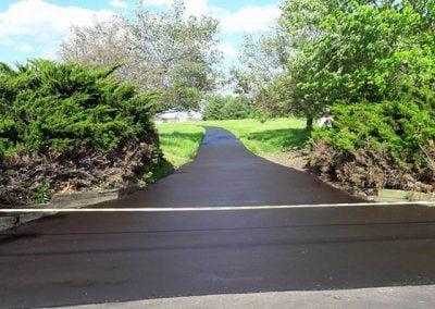 Paved path ends abruptly with a wooden barrier in a park-like setting.