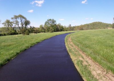A newly paved road curves through a green grassy field under a clear blue sky.