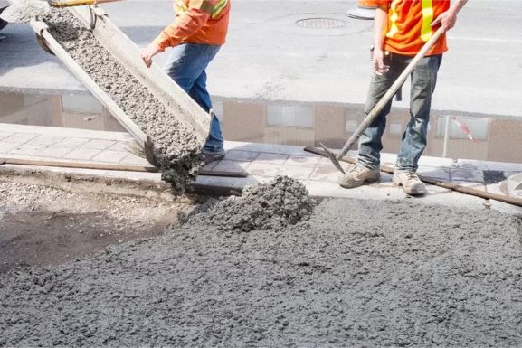 Construction workers pouring wet concrete onto a sidewalk.